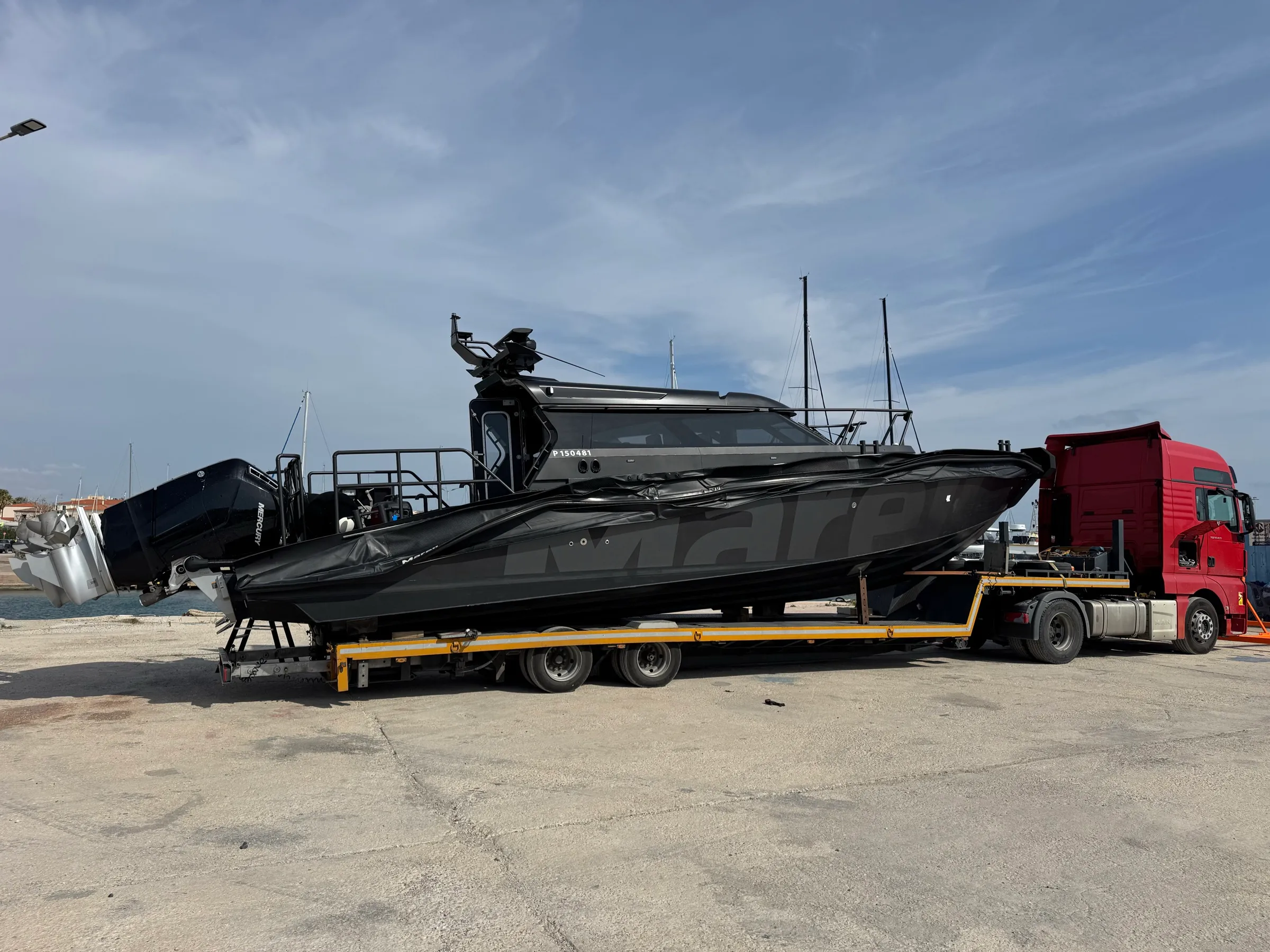 Sleek black Marex powerboat secured on a yellow low-loader trailer at a marina.